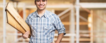 Portrait of a smiling carpenter holding wood planks in a construction site